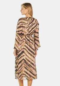 Lang, vloeiende jurk met een bruine, roze en crèmekleurige zigzagpatroon. Gemaakt van lichtgewicht stof met klokmouwen en een cinched taille.