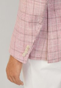 Blazer à carreaux rose clair avec une texture douce. Fini avec quatre boutons ronds de couleur claire sur le poignet. Coupe ajustée.