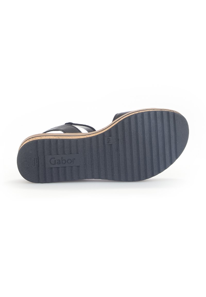 Sandale noire avec une semelle en caoutchouc texturé, présentant un design ajusté, plusieurs brides et une accent léger dans des tons beige le long du bord de la semelle.