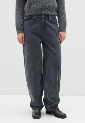 Pantalones de pana gris con corte de pierna ancha, que presentan rayas verticales y una cintura de altura media. Llevados con un suéter de punto gris y botas oscuras.