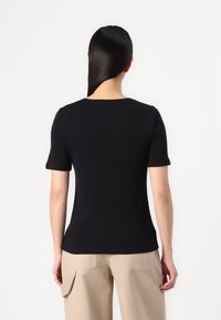 T-shirt nera a maniche corte con collo rotondo, silhouette aderente, texture morbida, design semplice, indossata con pantaloni cargo beige.