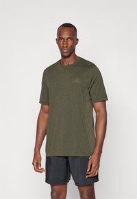 Camiseta deportiva verde oliva hecha de tejido texturizado, con mangas cortas y cuello redondo, combinada con pantalones cortos negros.