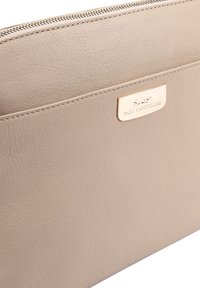 Beige leren tas met gouden rits en een metalen logo plaat met de tekst Paul Costelloe op het voorvak.