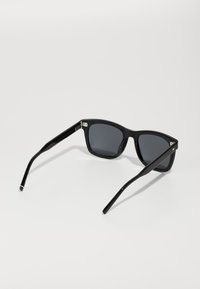Ochelari de soare din plastic negru cu lentile gri, cu rame rectangulare și brațe subțiri, având un accent subtil pe tâmplă.