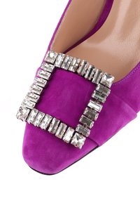 Pompa in suede viola con una fibbia quadrata di strass, caratterizzata da una punta affusolata e un rivestimento interno morbido. Suola nera piatta.