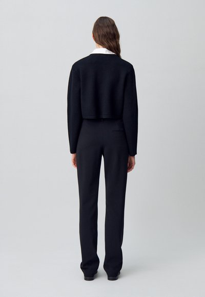 Maglione corto nero realizzato in tessuto a maglia, abbinato a pantaloni neri sartoriali. L'outfit presenta un design semplice senza modelli visibili.
