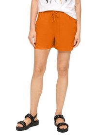 Oranje shorts met een elastische tailleband en trekkoord, gemaakt van zachte stof. Draag ze met zwarte gevlochten sandalen voor een casual look.
