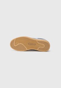 Podeszwa sneakersów Reebok z teksturowanym, tanowym gumowym podłożem, posiadająca heksagonalne wzory oraz wystającym logo Reebok, zaprojektowana z myślą o przyczepności i wsparciu.