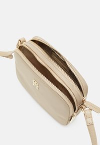 Beige læder crossbody taske med to lynlåslommer, guldfarvet hardware og en aftagelig rem. Glat tekstur og diskret design.
