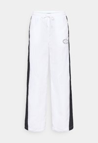 Bílé sportovní kalhoty s černými postranními pruhy. Obsahují elastický pás se šňůrkou a malé vyšívané logo na přední straně.