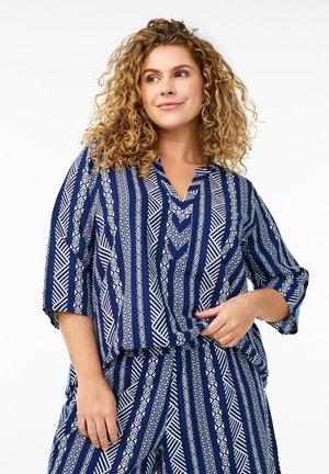 Navy and white patterned blouse with short sleeves, V-neckline, featuring geometric designs and a relaxed fit, paired with matching bottoms.