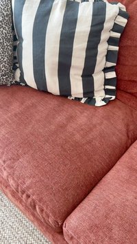 Rozsdabarna szövetkanapé, széles fekete és fehér függőleges csíkos párnával, fodros szélekkel.