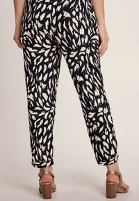 Zwarte en ivoorkleurige gestreepte broek met een relaxed fit, gemaakt van een textuurstof en met opgerolde manchetten. Draagt een paar tan hoge hakken.