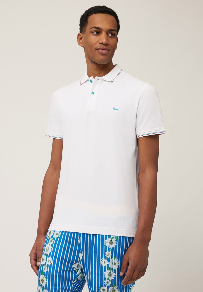 Polo bianco con colletto, dotato di un logo blu e bottoni. Rifinito con strisce multicolori. Abbinato a pantaloni corti blu a righe con motivi floreali.