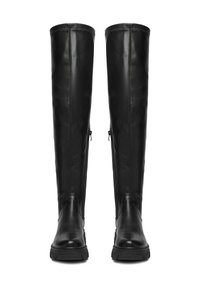 O pereche de cizme din piele negre, până la genunchi, cu fermoare laterale și talpă groasă cu striații, stând în poziție verticală pe un fundal alb.