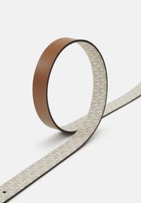 Cintura in pelle con un esterno marrone e un interno a fantasia crema. Presenta una texture liscia e un design elegante e minimalista.