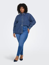 Camicia in denim blu scuro con chiusura a bottoni e colletto classico, abbinata a jeans skinny azzurri e décolleté blu con punta a punta.