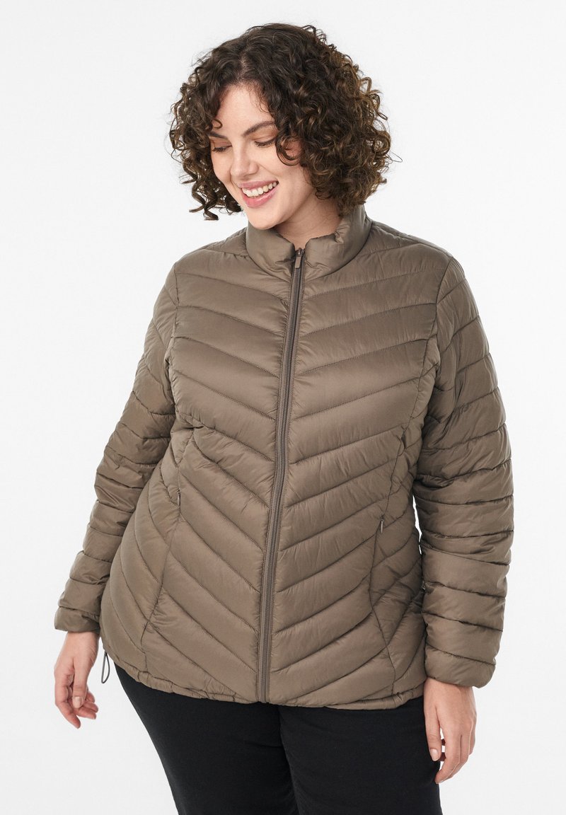 Padded jacket v zemitej hnedej farbe s stojatým golierom, šikmým švom a zipsovým uzáverom; má hladkú, ľahkú štruktúru.