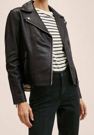 Osoba nosząca czarną skórzaną kurtkę motocyklową na białej i czarnej koszulce w paski, w połączeniu z czarnymi jeansami z wysokim stanem.