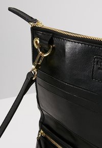 Pochette en cuir noir avec fermeture éclair dorée, attache à clip dorée et plusieurs emplacements pour cartes à l'intérieur.