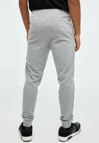 Pantalones de chándal de algodón gris con piernas cónicas y puños elásticos, combinados con zapatillas negras. Diseño sencillo, sin patrones ni herrajes visibles.