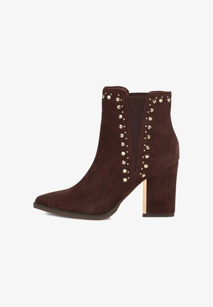 Bottines en daim marron avec un bout pointu, accents en clous dorés sur les côtés, et un talon épais avec un détail métallique à la base.