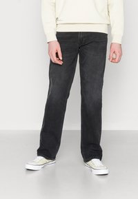 Jeans de mezclilla negra con corte recto, usados con un sudadera color crema y zapatillas de color claro. Textura suave y detalles mínimos.