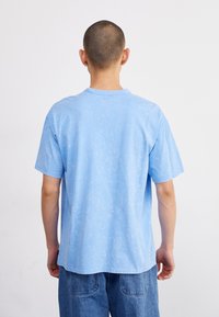 Γαλάζιο βαμβακερό μπλουζάκι με χαλαρή γραμμή, στρογγυλή λαιμόκοψη, κοντά μανίκια και ελαφρώς υφασμένο φινίρισμα, θέα από πίσω.