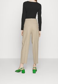 Top nero a maniche lunghe, pantaloni beige a vita alta e sandali con tacco verde dal design intrecciato e tacchi quadrati.