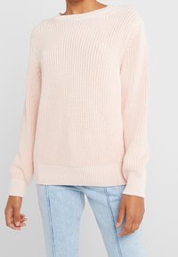 Pull tricoté rose clair avec une texture côtelée, un col rond et des manches longues. L'ourlet et les poignets sont également côtelés.