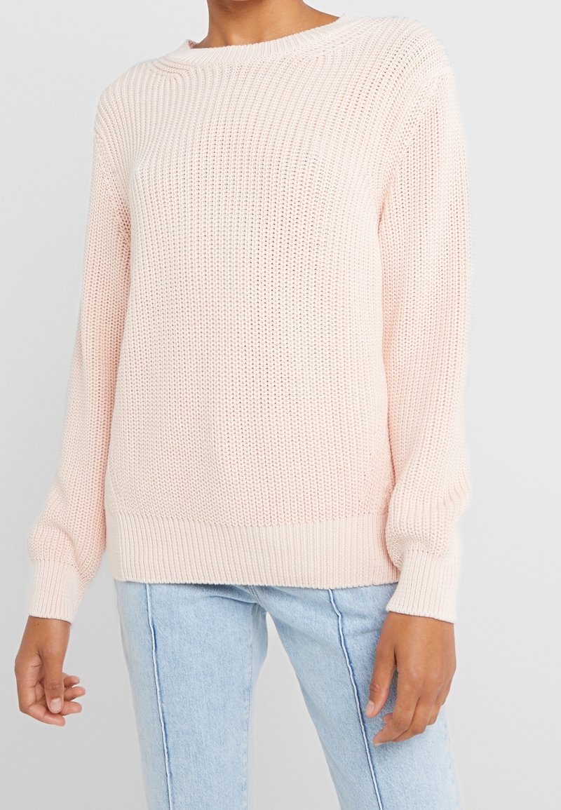 Pull tricoté rose clair avec une texture côtelée, un col rond et des manches longues. L'ourlet et les poignets sont également côtelés.