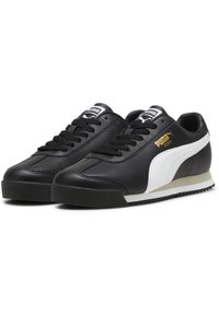 Baskets en cuir noir avec une bande latérale blanche, des accents de logo dorés, un bout rond et une semelle extérieure en caoutchouc texturée. Fermeture à lacets à l'avant et col rembourré.