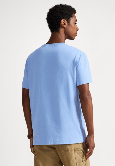 Ανοιχτό μπλε βαμβακερό μπλουζάκι με κοντά μανίκια, στρογγυλή λαιμόκοψη και άνετη γραμμή· η πίσω όψη δεν έχει ιδιαίτερες λεπτομέρειες και δεν εμφανίζει ορατά σχέδια.