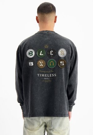 Zwarte longsleeve-shirt van vintage-stijl stof, met een grafische print van negen cirkelvormige ontwerpen in verschillende kleuren en de tekst "Timeless".