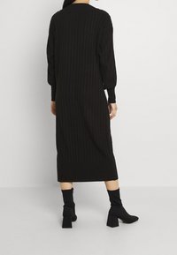 Abito nero lavorato a maglia con texture a coste, maniche lunghe e taglio a metà lunghezza, abbinato a stivali neri tipo calza con tacco quadrato.