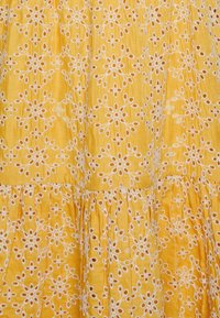 Tissu jaune avec motif floral découpé brodé blanc et détail de couture froncée.