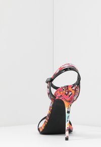 Sandalo con tacco alto caratterizzato da un motivo astratto colorato, cinturini in vernice nera e un tacco a stiletto con finitura testurizzata.
