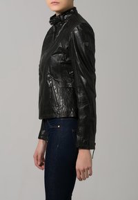 Giacca di pelle nera con colletto alto, cerniera frontale e tasche laterali. Superficie testurizzata e design aderente, mostrata di lato.