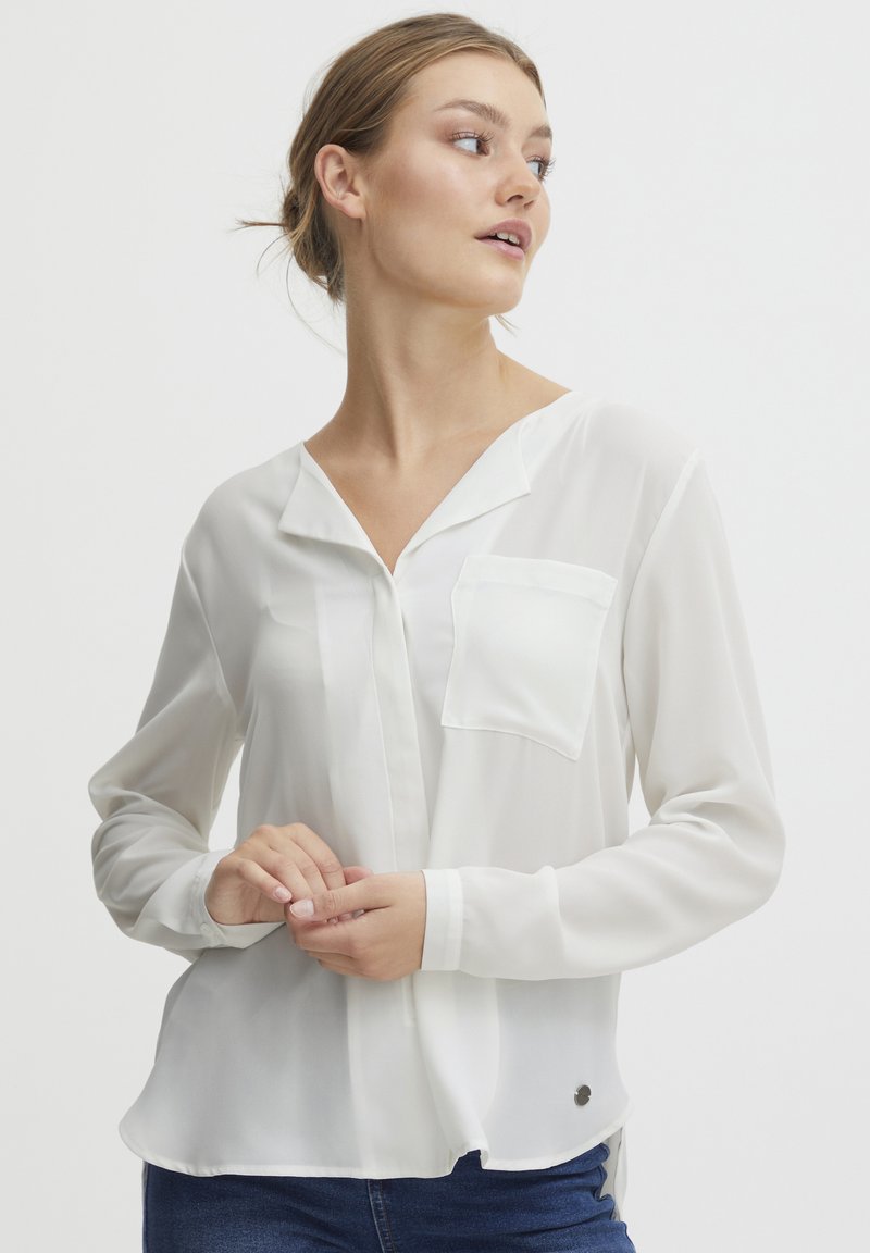 Blusa bianca a maniche lunghe in tessuto leggero con tasca sul petto sinistro e orlo curvo. Presenta una chiusura con bottoni e una morbida consistenza.