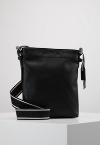 Borsa a tracolla in pelle nera con hardware argentato, tracolla regolabile a righe e design minimalista con un piccolo etichetta.