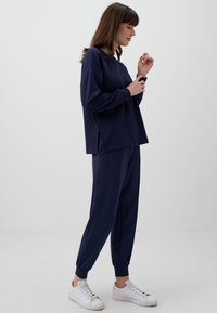 Granatowy sweatshirt i pasujące dresy wykonane z miękkiego materiału. Sweatshirt ma luźny krój z bocznymi rozcięciami, podczas gdy spodnie mają elastyczne ściągacze.