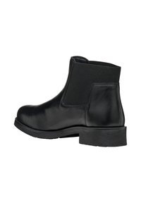 Bottine en cuir noir avec des panneaux latéraux élastiques, bout arrondi et petit talon texturé. Fini lisse avec des détails de couture minimalistes.