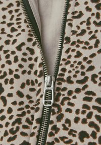 Gros plan sur une veste imprimée léopard partiellement zippée avec une fermeture éclair en métal et une peau visible sur la poitrine en dessous.