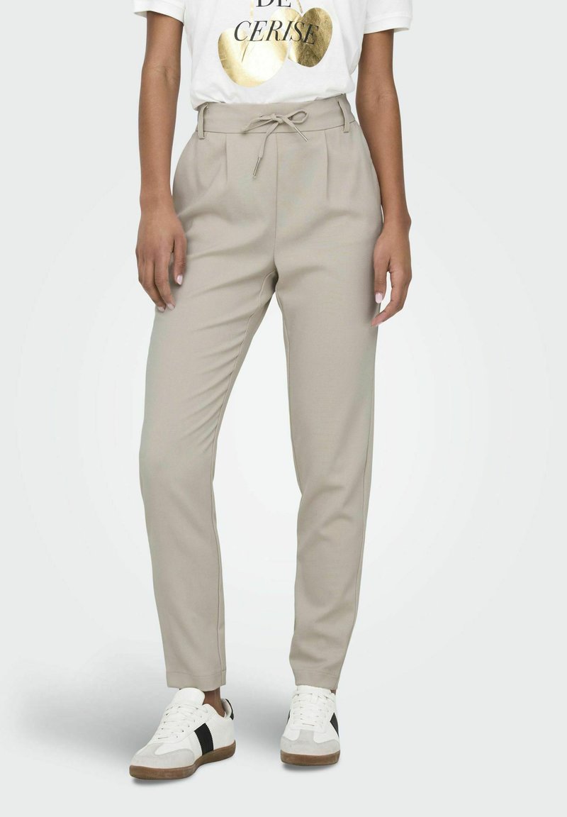 Pantalons beiges fuselés avec une taille à cordon, associés à un t-shirt graphique blanc et des baskets blanches avec des accents noirs.