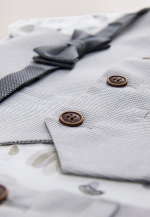 Hall tooniga tekstuuriga kangast ülikond koos kikilipsuga, millel on pruunid nööbid ja lillemustriline vooder. Lähedalt vaadates detailid ja kangad.