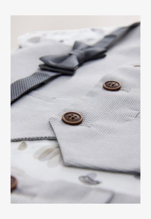 Szary garnitur z tkaniny o fakturze, z muszką, ozdobiony brązowymi guzikami i podszewką w kwiatowy wzór. Zbliżenie na detale i tkaniny.