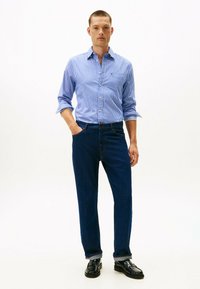 Blå og hvid stribet skjorte med knapper, parret med mørkeblå jeans og sorte lædersko. Skjorten har lange ærmer og en krave.