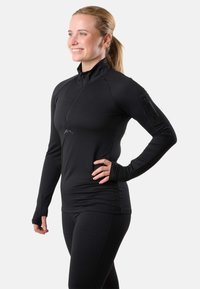 Maglietta atletica nera a maniche lunghe con mezza cerniera e fori per il pollice, dotata di una tasca con cerniera sul braccio sinistro e di un logo discreto sul petto.