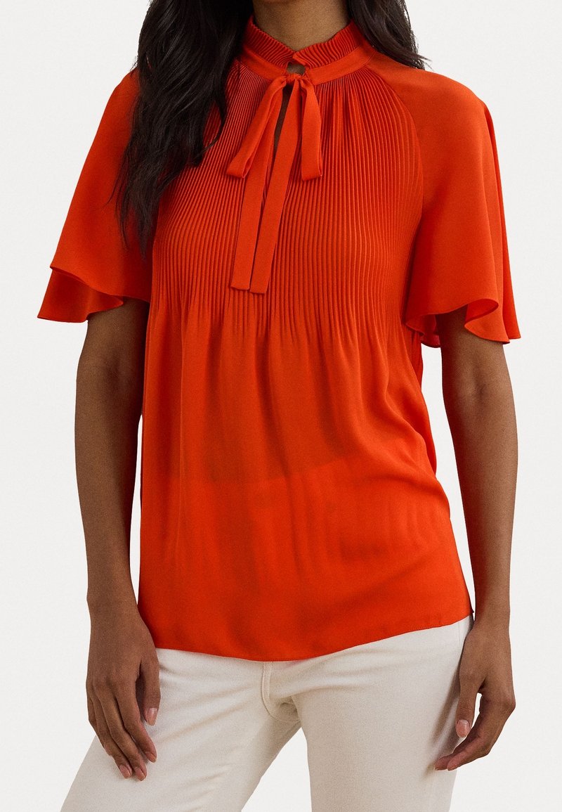 Red short-sleeve blouse with pleated texture, keyhole neckline, and ribbon tie detail. Smooth fabric, relaxed fit, and flared sleeves.