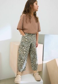 Barna oversize póló, bézs és fekete leopárdmintás, széles szárú nadrág, és bézs mokaszin stílusú cipők.